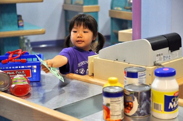 A child pretending to buy items at a toy grocery store.